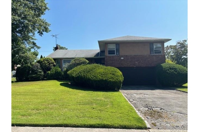 View of front of property with an attached garage, brick siding, a front yard, and driveway