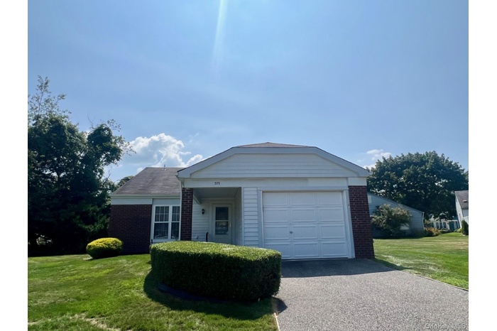 View of front of home with brick siding, a front lawn, an attached garage, and driveway