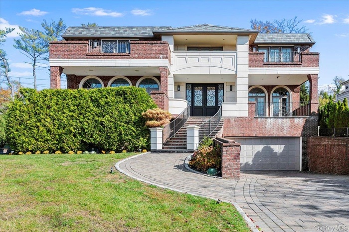 View of front of house with a balcony, french doors, brick siding, a garage, and decorative driveway