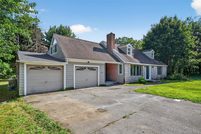Cape cod-style house with driveway, a chimney, and a front yard