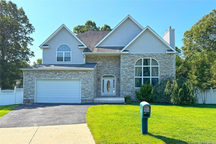 View of front of home featuring an attached garage, asphalt driveway, stone siding, and a chimney