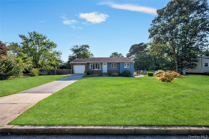 Single story home featuring driveway, brick siding, a chimney, and a garage