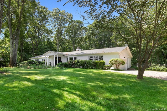 Single story home featuring a front yard, an attached garage, a chimney, and view of scattered trees