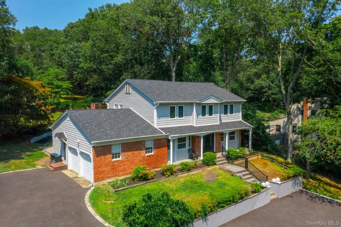 View of front of property featuring a shingled roof, an attached garage, asphalt driveway, brick siding, and a porch