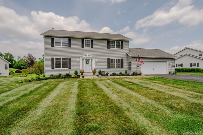 Colonial home with asphalt driveway, an attached garage, and a front lawn