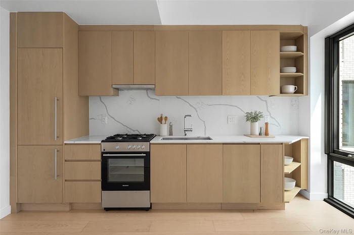 Kitchen with open shelves, modern cabinets, stainless steel range with gas cooktop, light brown cabinets, and tasteful backsplash