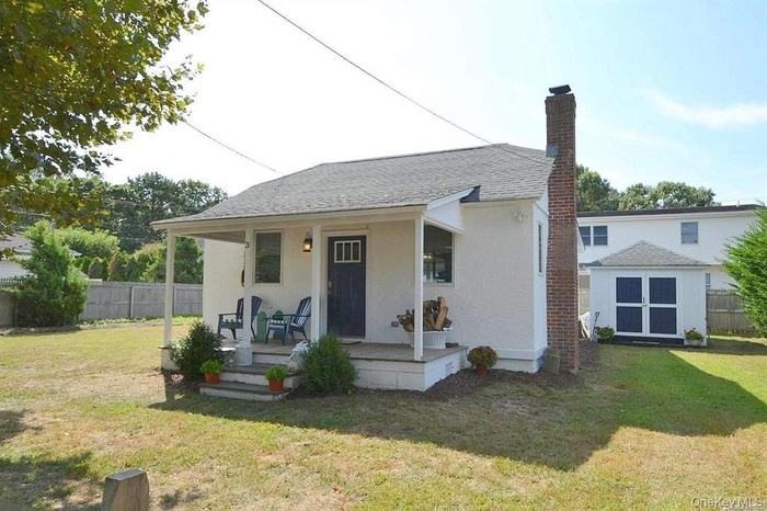 View of front of property with covered porch, a chimney, stucco siding, and a shingled roof