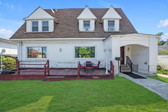 View of front facade with a shingled roof, a front lawn, and a wooden deck