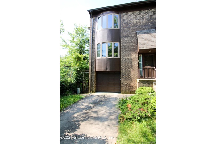 View of front of house featuring driveway, an attached garage, brick siding, and a balcony