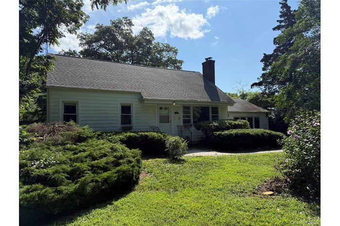 View of front of home featuring a front yard, a shingled roof, and a chimney
