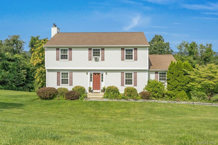 Colonial house featuring a chimney, a front yard, and a shingled roof