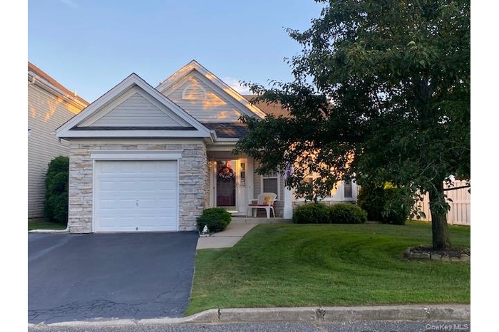 View of front of home with an attached garage, asphalt driveway, covered porch, and stone siding