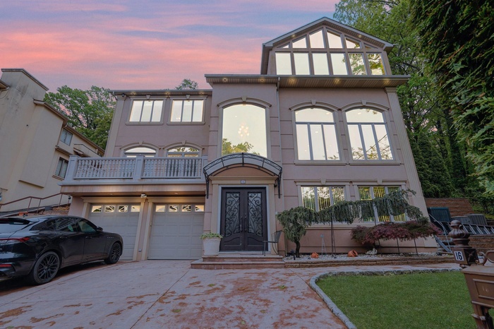 View of front of property with concrete driveway, stucco siding, a balcony, a garage, and french doors