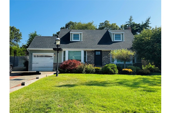Cape cod-style house with stone siding, a garage, a front yard, and roof with shingles