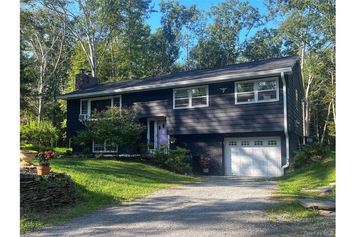 Split foyer home featuring a garage, driveway, a chimney, brick siding, and a front yard