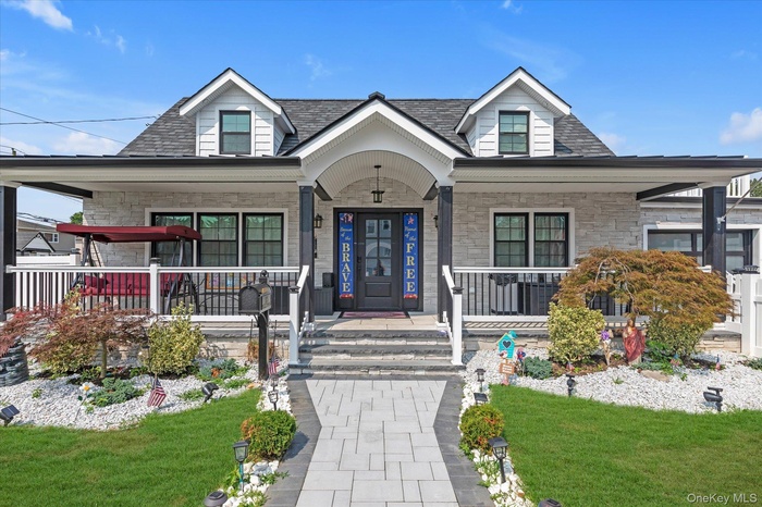 View of front of home featuring a porch, stone siding, a front yard, and a shingled roof