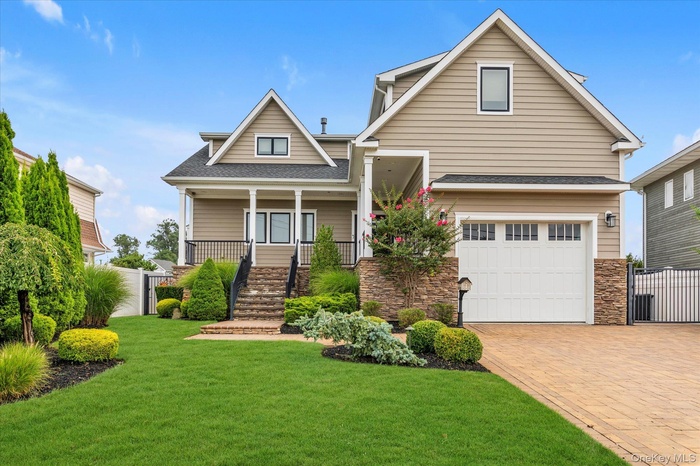 View of front facade with a garage, a shingled roof, stone siding, a porch, and decorative driveway
