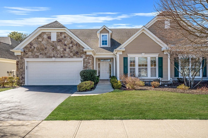 View of front facade with stone siding, concrete driveway, a front lawn, a shingled roof, and a garage