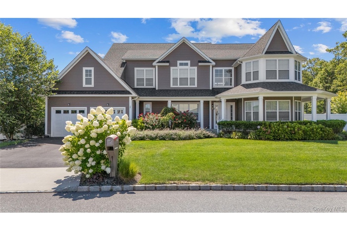 View of front facade featuring a front lawn, a porch, a shingled roof, driveway, and a garage