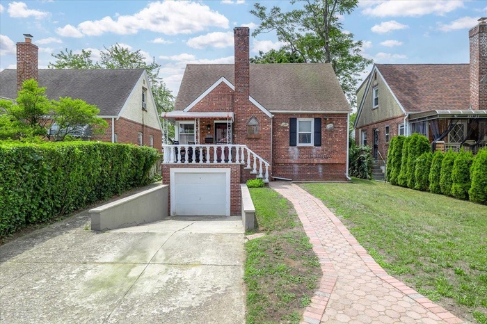 Tudor house featuring brick siding, concrete driveway, a front lawn, a chimney, and a garage