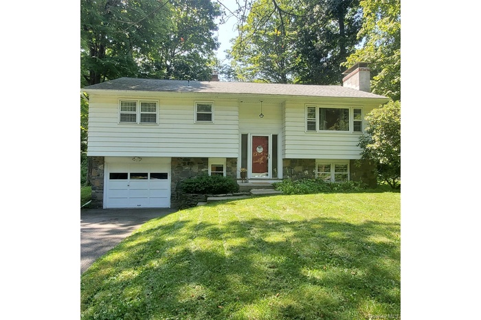 Split foyer home featuring an attached garage, a chimney, a front yard, stone siding, and asphalt driveway