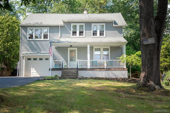 View of front of property with a garage, driveway, a shingled roof, a chimney, and covered porch