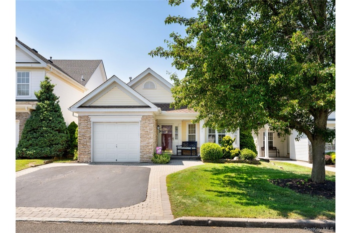 View of front of home featuring asphalt driveway, an attached garage, a front yard, covered porch, and stone siding
