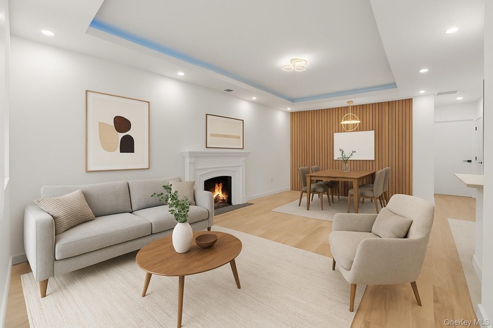 Living room with a tray ceiling, recessed lighting, a fireplace with flush hearth, and light wood finished floors