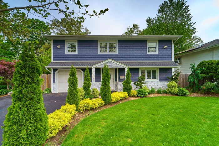 View of front of house with stone siding, driveway, a garage, and a shingled roof
