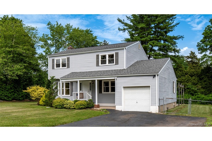 Traditional-style home with a chimney, an attached garage, a shingled roof, asphalt driveway, and covered porch