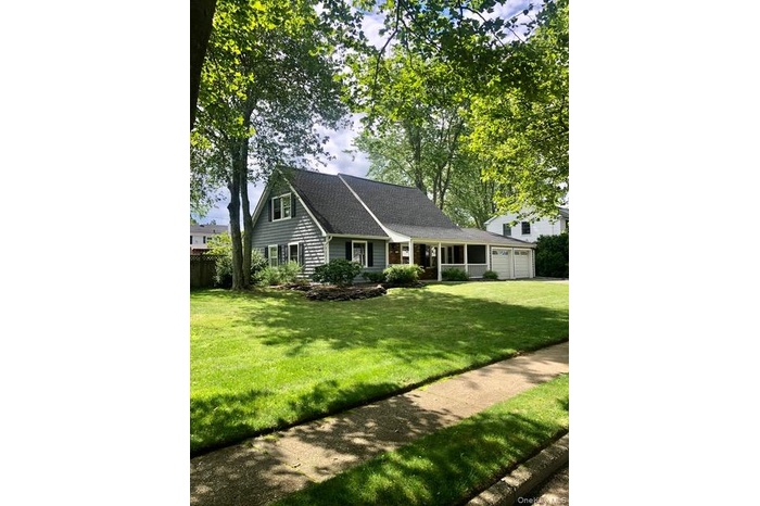 View of front of home with roof with shingles, a front yard, and a garage
