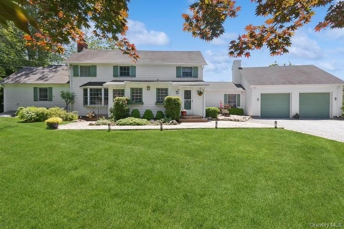 View of front facade with a front yard, an attached garage, a chimney, and driveway