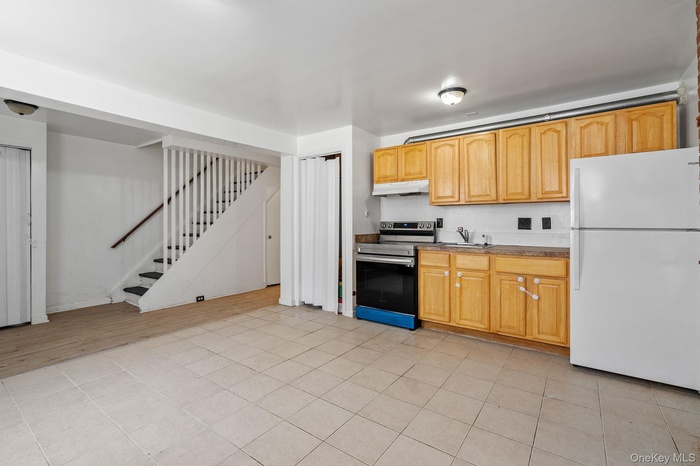 Kitchen with freestanding refrigerator, stainless steel electric stove, light tile patterned floors, and under cabinet range hood