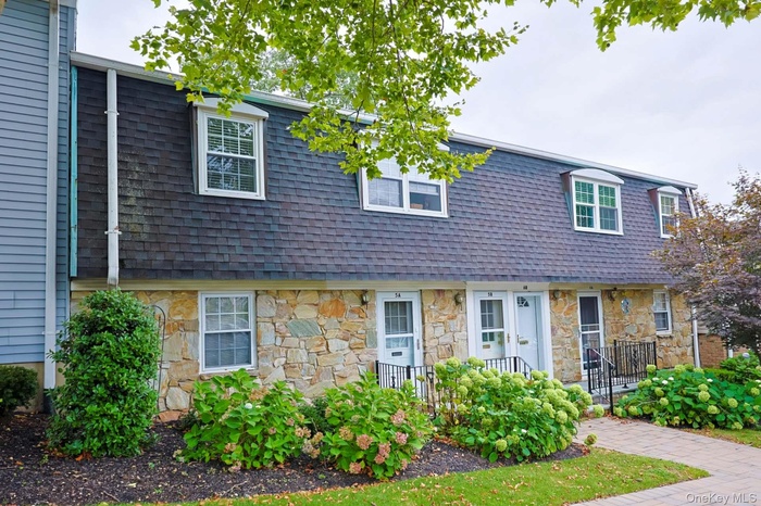 View of front of property with mansard roof, stone siding, and a shingled roof