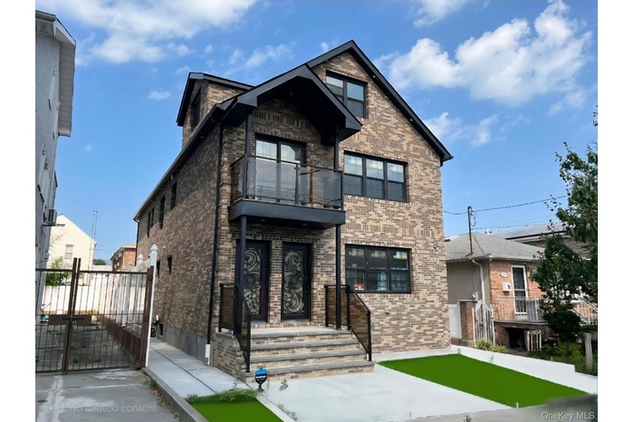 View of front of property featuring a balcony, brick siding, and a gate