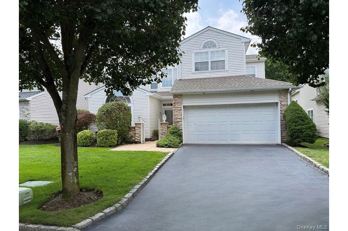 View of front of home with stone siding, roof with shingles, asphalt driveway, an attached garage, and a front lawn