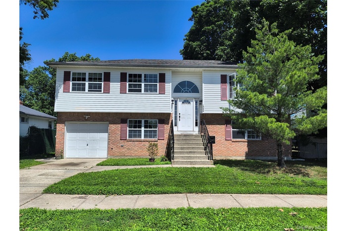 Split foyer home with an attached garage, concrete driveway, a front yard, and brick siding
