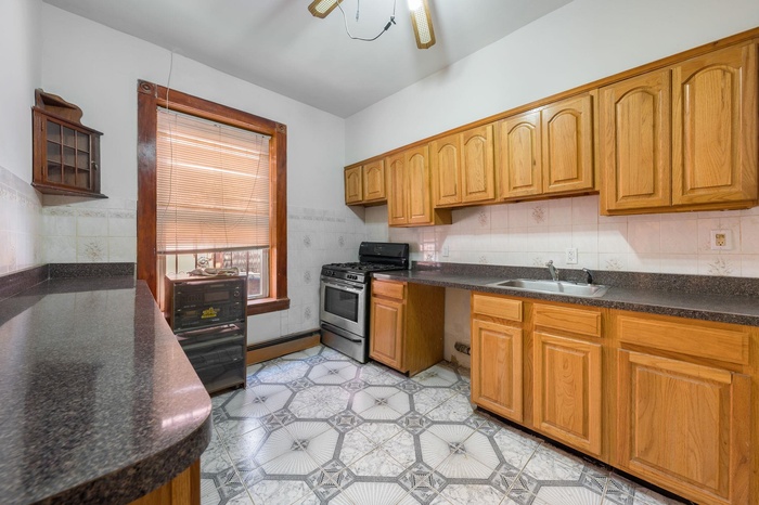 Kitchen featuring stainless steel range with gas cooktop, a ceiling fan, dark countertops, a baseboard radiator, and brown cabinetry