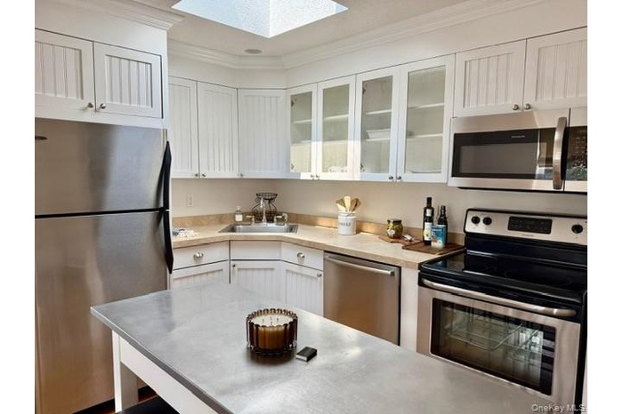Kitchen featuring appliances with stainless steel finishes, light countertops, crown molding, white cabinetry, and glass insert cabinets