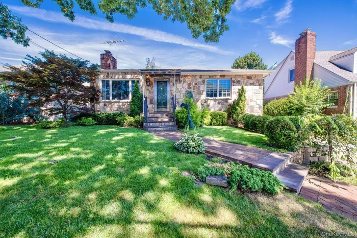 View of front of property with a front lawn, stone siding, and a chimney