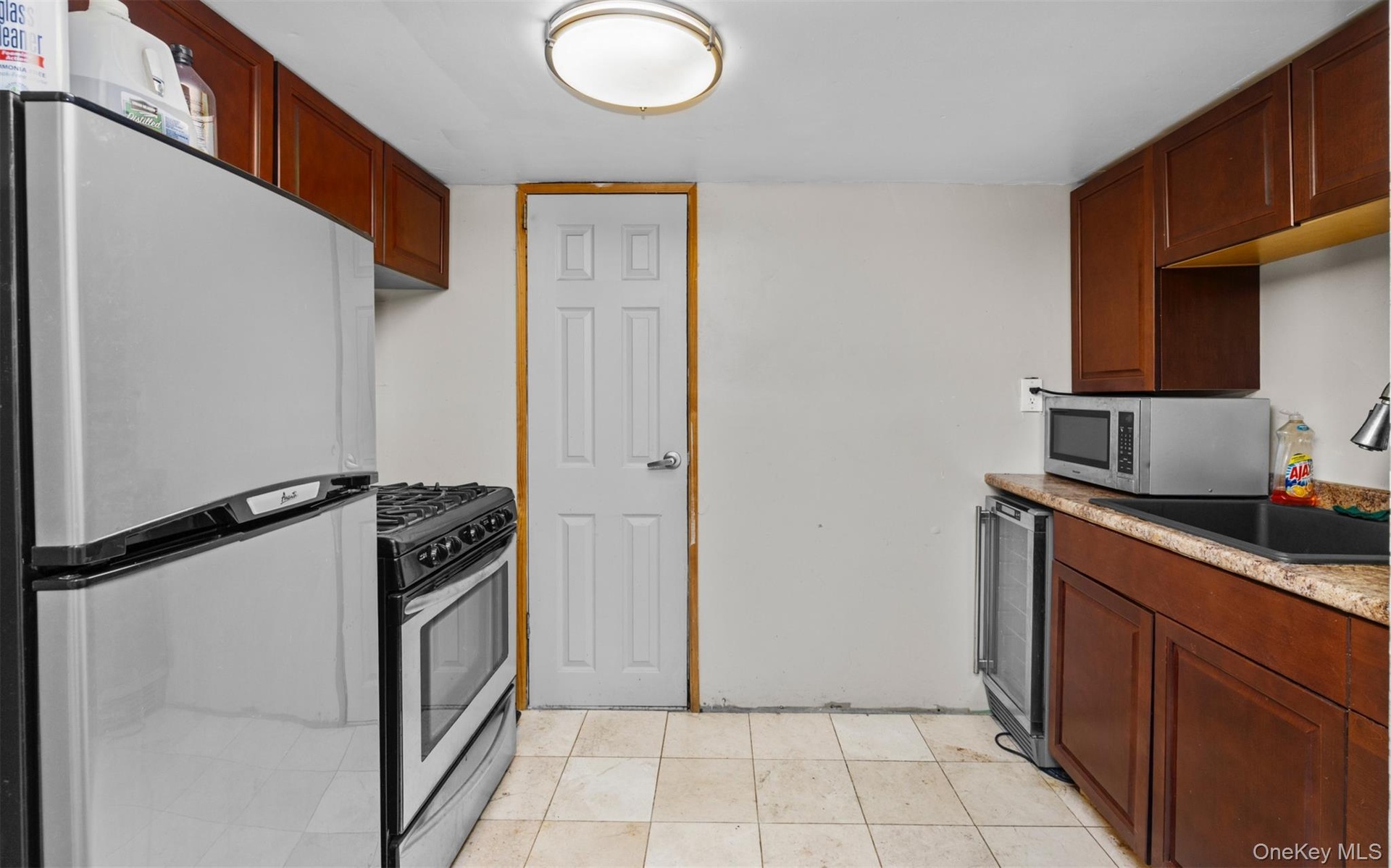 Kitchen featuring appliances with stainless steel finishes, light tile patterned floors, light stone countertops, and beverage cooler