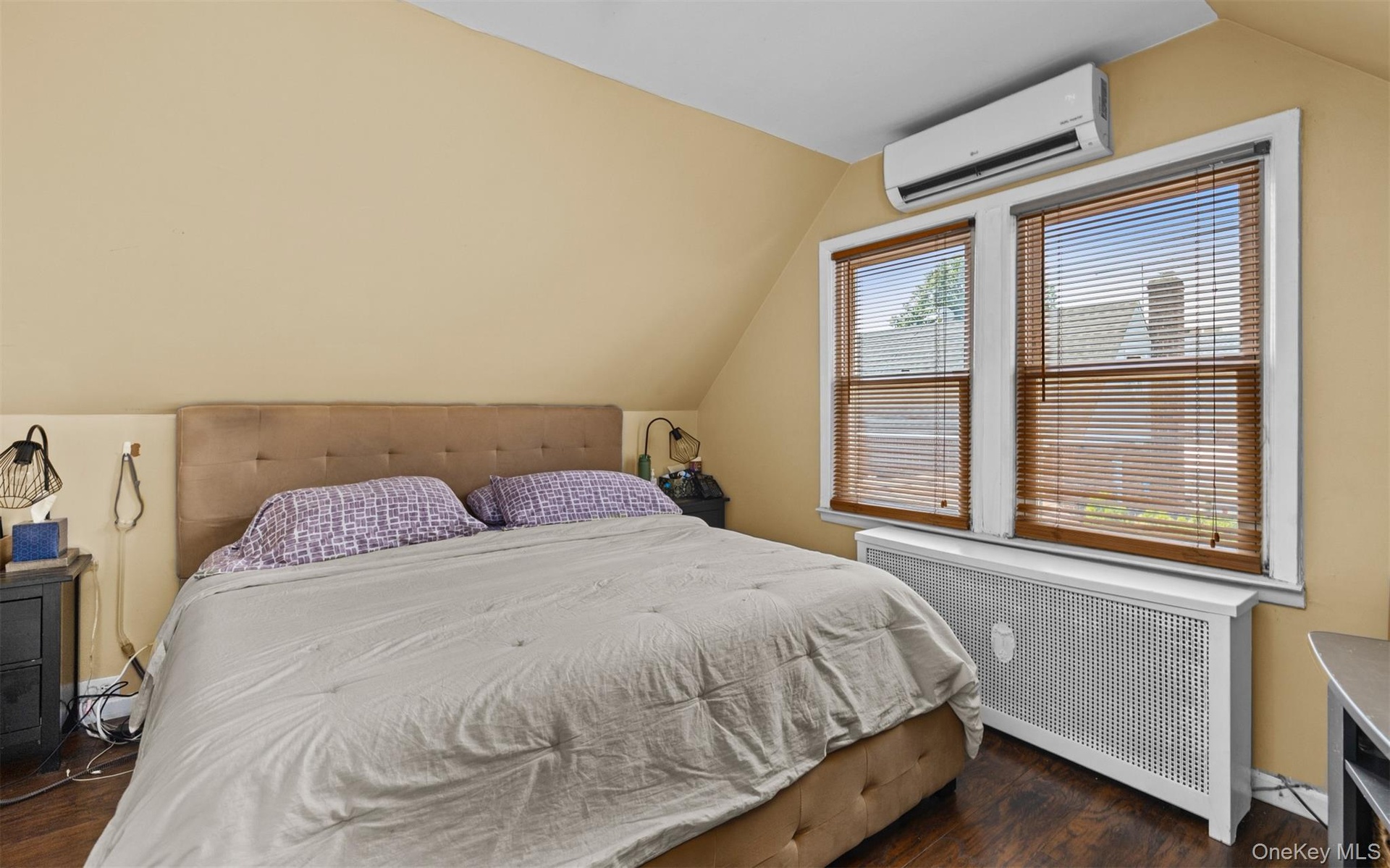 Bedroom with radiator, lofted ceiling, dark wood-style flooring, and a wall mounted air conditioner