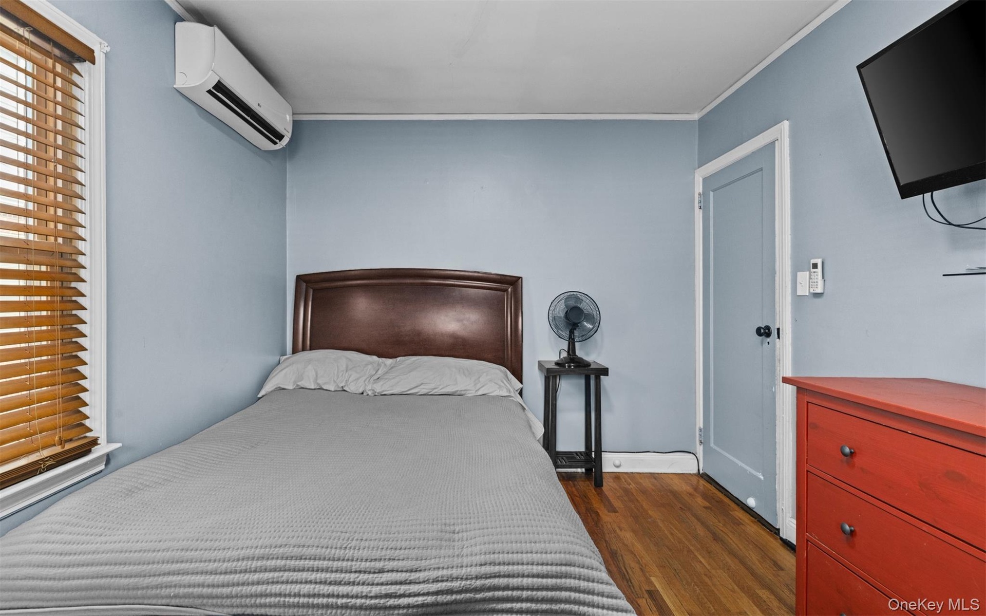 Bedroom with dark wood-style floors, an AC wall unit, and ornamental molding