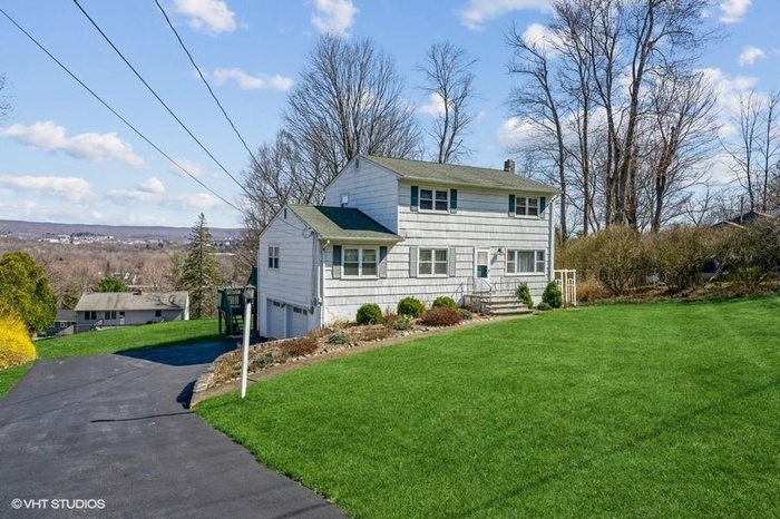 View of front of property featuring asphalt driveway, an attached garage, a chimney, and a front lawn