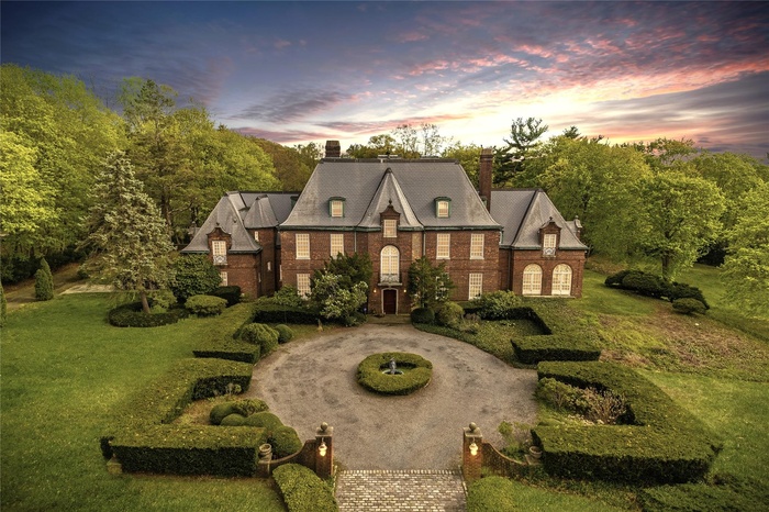 View of front facade with curved driveway, a chimney, and a lawn