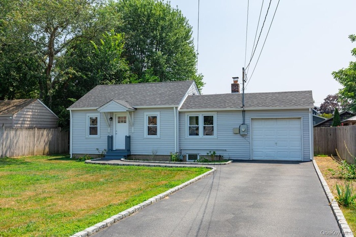 View of front of home featuring an attached garage, a chimney, asphalt driveway, and roof with shingles