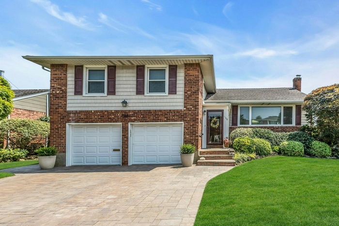 Tri-level home featuring decorative driveway, an attached garage, a front lawn, and brick siding