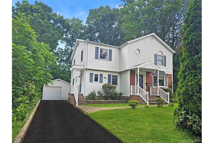 Colonial inspired home featuring an outbuilding, a garage, a front lawn, and asphalt driveway