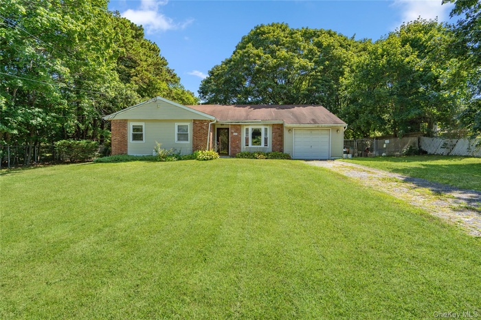 Ranch-style house with driveway, brick siding, a garage, and view of wooded area