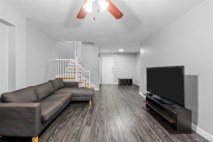 Living area with stairs, dark wood-type flooring, and ceiling fan